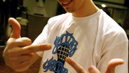 In einem T-Shirt mit dem Gitter Spitter Records-Logo posiert MC Eklat mit zwei Mittelfingern. © Steffen Kugler / dpa / picture alliance Foto: Steffen Kugler