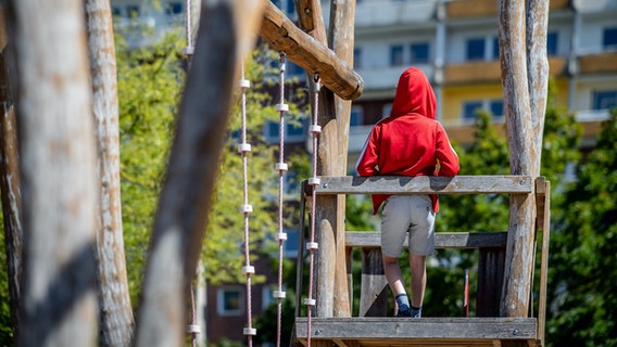 Ein Kind steht auf einem Spielplatz vor einem Plattenbau. © Thomas Eisenhuth / picture alliance Foto: Thomas Eisenhuth