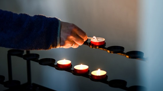 Das Bild zeigt eine Hand mit einen Streichholz, die ein Teelicht in einer Kirche anzündet. © Photocase Foto: David W.