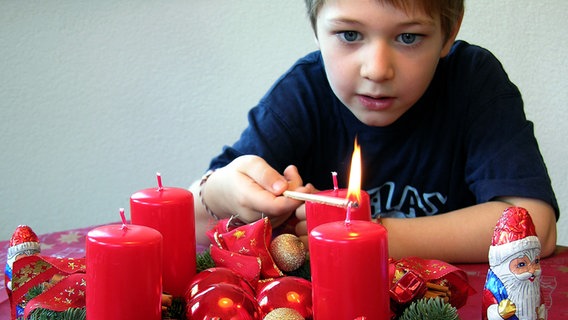 Ein kleiner Junge zündet mit großen Augen die erste Kerze auf dem Adventskranz an. © picture-alliance/ dpa Foto: Jürgen Effner