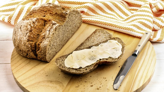 Brotlaib und eine abgeschnittene Scheibe mit Butter bestrichen © JB/Shotshop/picture alliance 