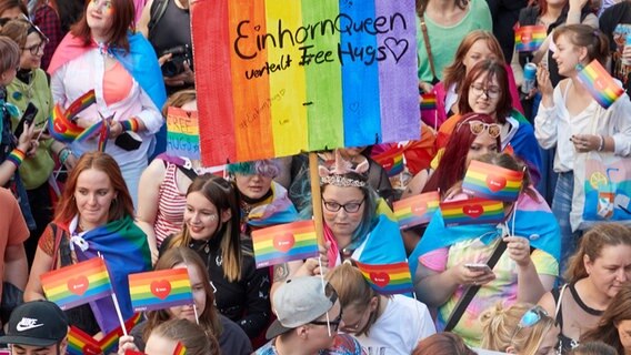 Menschen schwenken kleine Regenbogenflaggen bei einer Parade. © picture alliance/dpa Foto: Georg Wendt