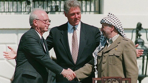 Der ehemalige Israels Premierminister Jitzchak Rabin (li.) und Palästinenser-Präsident Jassir Arafat (re.) bei dem historischen Händeschütteln am Weißen Haus - zusammengeführt von US Präsident Bill Clinton (1993). © picture-alliance / dpa Foto: Avi_Ohayon-Israeli_Government_Pr