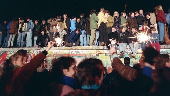 Einen Tag nach der Grenzöffnung in Berlin feiern tausende Menschen auf, vor und hinter der Berliner Mauer am Brandenburger Tor, aufgenommen am 10. November 1989 auf West-Berliner Seite. © picture-alliance/ ZB Foto: Peter Zimmermann