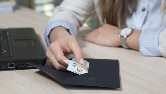 Eine Frau zieht Geldscheine aus einem Umschlag der auf ihrem Schreibtisch liegt. © panthermedia Foto: YAY Micro