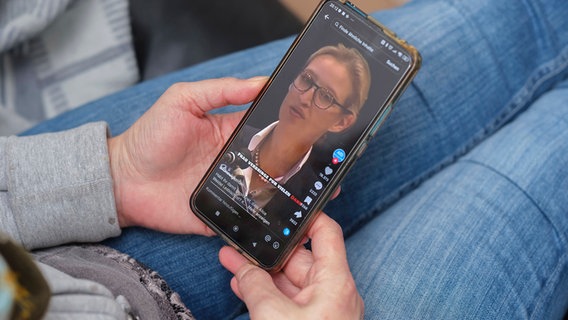 Frau hält ein Mobiltelefon auf dessen Display auf der Plattform TikTok ein Video der AfD Politikerin Alice Weidel zu sehen ist. © imago 