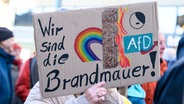 Eine Frau hält auf einer Demonstration ein Pappschild vor ihr Gesicht, auf dem "Wir sind die Brandmauer" steht. © Salome Roessler/dpa +++ dpa-Bildfunk +++ 