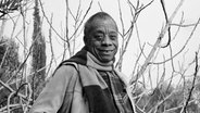 Der Schriftsteller James Baldwin auf einem Schwarz-Weiß-Foto draußen vor kahlen winterlichen Ästen. © picture alliance Foto: -