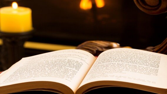 Ein aufgeschlagenes Buch liegt neben einer brennenden Kerze. © Fotolia Foto: steheap