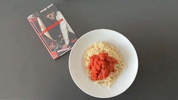 Ein Buch liegt neben einem Teller mit Spaghetti mit Tomatensoße. © NDR Foto: Andrea Velleuer