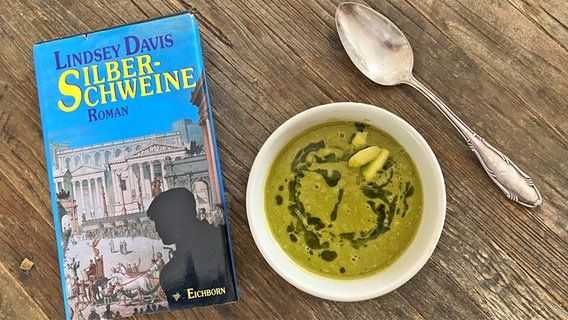 Ein Roman von Lindsey Davis "Silberschweine" neben einer grüngelben Suppe und einem Silberlöffel - eat.READ.sleep Folge 26 © NDR Foto: Daniel Kaiser