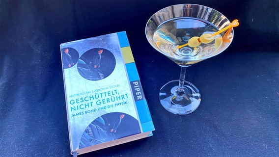 ein Martini-Glas mit Olive neben dem Buch "Gerührt, nicht geschüttelt" - Folge 33 des Podcasts eat.READ.sleep © NDR Foto: Katharina Mahrenholtz