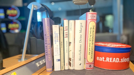 Verschiedene Bücher stehen in einem Podcast-Studio neben einer Box, die mit eat.READ.sleep.-Slogan beklebt ist. © NDR Foto: Katharina Mahrenholtz