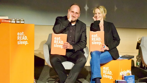 Daniel Kaiser und Katharina Mahrenholtz sitzen nebeneinander und haben eat.READ.sleep.-Bücher auf dem Schoß. © NDR 