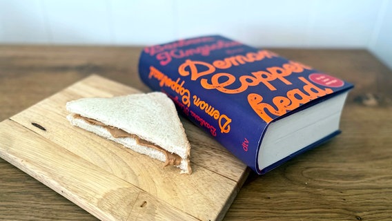 Ein Sandwich liegt auf einem Bretten, daneben ein dickes Buch - Bild zu Folge 108 von eat.READ.sleep. © NDR Foto: Katharina Mahrenholtz