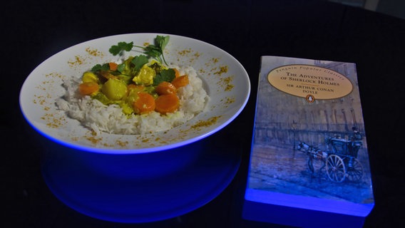 Ein Teller mit Curry-Gemüse und Reis neben "Sherlock Holmes" - dem Krimi von Arthur Conan Doyle - Folge 53 von eat READ sleep © NDR Foto: Tim Piotraschke