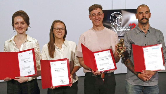 Vier Autoren, die beim Bachmann-Wettbewerb teilnahmen, halten ihre Urkunden hoch. © picture alliance/dpa/APA | Gert Eggenberger 