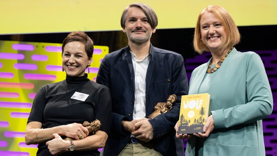 Die Illustratorin Regina Kehn und der Autor Sasa Stanisic nehmen den Jugendliteraturpreis für ihr Kinderbuch "Wolf" entgegen. Rechts steht Bundesfamilienministerin Lisa Paus. © picture alliance/dpa | Boris Roessler Foto: picture alliance/dpa | Boris Roessler