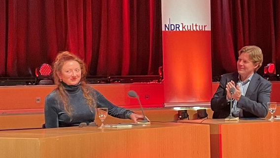 Der NDR Redakteur Jan Ehlert applaudiert der Schriftstellerin Claire Keegan auf einem Podium. © NDR Foto: Jens Büchsenmann