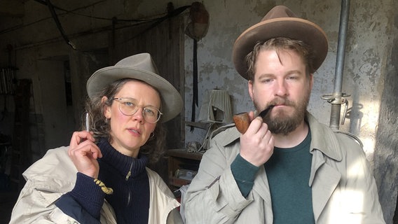 Ein Mann und eine Frau posieren in Trenchcoat und Hut mit Zigarette und Pfeife als Kommissare. © NDR Foto: Patrick Eicke