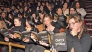 Viele jüngere Frauen in einem Lesesaal des Rathauses von New York halt einen Roman mit schwarzen Cover aufgeschlagen und lesen darin: Es ist Rebecca Yarros' Bestseller "Onyx Storm" © picture alliance / CJ Rivera/Invision/AP | CJ Rivera Foto:  CJ Rivera