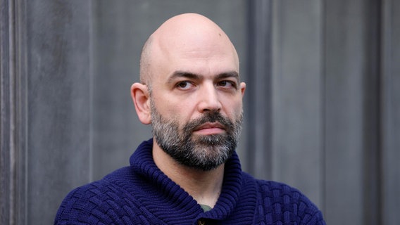 Porträtfoto von Roberto Saviano vor einer grauen Wand. Er trägt einen blauen Strickpullover. © picture alliance / ANSA | FABIO FRUSTACI 