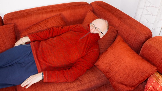 Abbildung aus "Das Ende der Unsterblichkeit" von Mario Wezel: Ein Mann mit einem roten Pullover schläft auf einem roten Sofa © Fotohof / Mario Wezel 