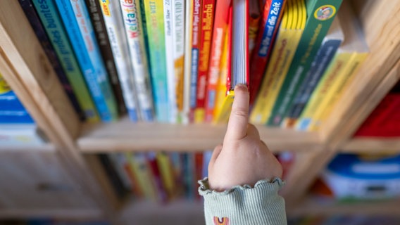 Eine Kinderhand zieht ein Buch aus einem Bücherregal. © picture alliance/dpa | Hendrik Schmidt 