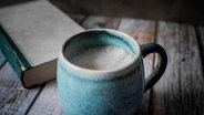 Eine Kaffeetasse und ein altes Buch auf einem Holztisch. © picture alliance / Zoonar | Linda Brotkorb 