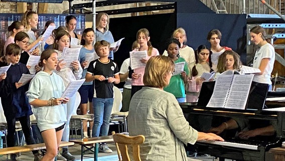 Jugendliche stehen in einer Halle und singen, davor sitzt eine Frau am Klavier © NDR / Linda Ebener Foto: Linda Ebener