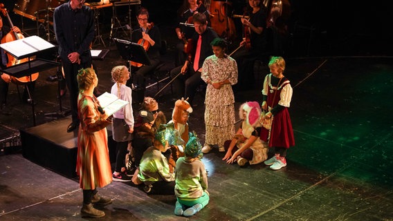 Verkleidete Kinder stehen auf einer Theaterbühne inmitten von Orchestermusiker*innen © Olaf Struck 