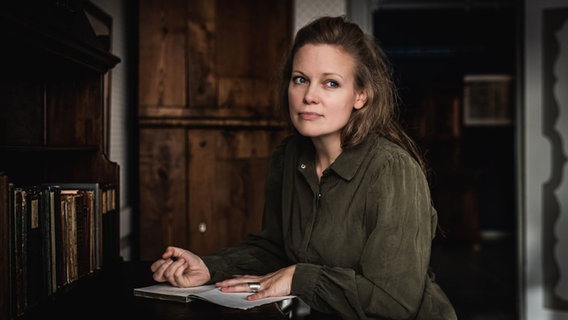 Eine Frau sitzt nachdenklich an einem Schreibtisch und hält einen Stift in der Hand. © Jörg Petersen Foto: Jörg Petersen