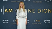 Celine Dion steht bei der Filmpremiere von "I Am: Celine Dion" in einem weißen Kleid vor einer Werbetafel. © picture alliance / NDZ/STAR MAX/IPx | NDZ/STAR MAX/IPx 