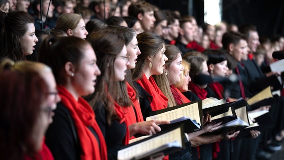 Eine Gruppe junger Menschen in schwarzen Gewändern mit roten Schals singt beim Chorwettbewerb in Leipzig © picture alliance/dpa | Hendrik Schmidt Foto: Hendrik Schmidt