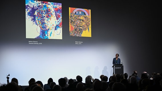 Naomi Beckwith steht auf einer Bühne im Hintergrund sind zwei Werke von Nelson Stevens zu sehen. © picture alliance/dpa | Uwe Zucchi Foto: Uwe Zucchi