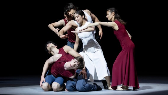 Zwei Tänzerinnen und zwei Tänzer strecken ihre Arme nach unten, wo zwei Menschen auf dem Boden knien - Szene aus John Neumeiers "Epilog" © Kiran West 