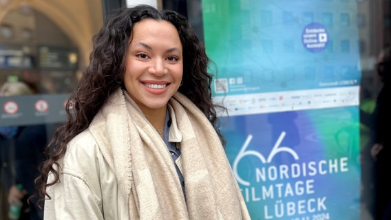 Eine junge Frau mit dunklen Locken und langen offenen Haaren lächelt vor einem Kino in Lübeck bei den Nordischen Filmtagen © NDR Foto: Patricia Batlle