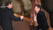 Ein Mann im schwarzen Smoking überreicht einen Oscar an einen anderen, etwas kleineren Mann, der dabei lacht - Quentin Tarantino (links) überreicht Sean Baker den Oscar als bester Regisseur bei der Oscar-Gala 2025 © Chris Pizzello/Invision/AP/dpa +++ dpa-Bildfunk +++ Foto: Chris Pizzello