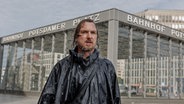 Ein Mann in grün gekleidet mit nassen Haaren steht im Regen an einer Berliner Kreuzung - Szene aus dme Film "Das Licht" © Frédéric Batier / X Verleih AG Foto: Frédéric Batier