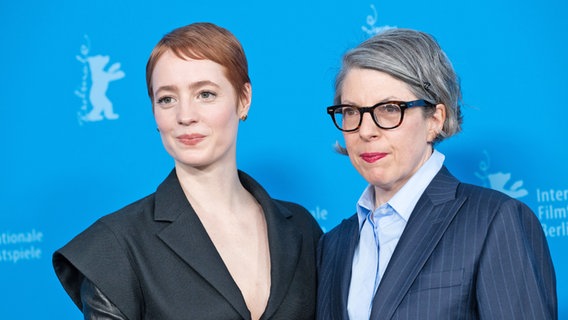 eine junge Frau mit kurzen Haaren und schwarzem Kleid steht neben eine etwas älteren mit Bubi-Schopf und Brille mit blauem Hemd und Sakko © Berlinale 2025 / Ali Ghandtschi Foto: Ali Ghandtschi