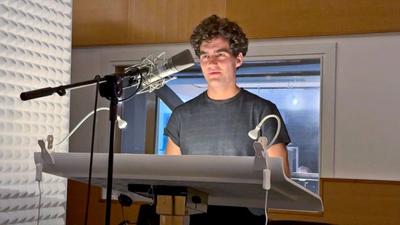 Hombre de pelo oscuro hablando de su papel en el estudio de doblaje (Pascal Hudos en el estudio de grabación con micrófono) © NDR Foto: Kai Salander