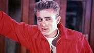 James Dean trägt eine rote Jacke und blicket verwegen. © Picture-Alliance / Photoshot | Bandphoto 