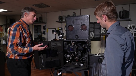 Andreas Dobelmann (l.) zeigt einem Besucher ein Filmvorführgerät. © Screenshot NDR 