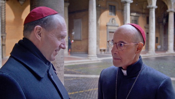 Zwei Geistliche unterhalten sich in einem Hof des Vatikans miteinander - Szene aus Edward Bergers Film "Konklave" mit Ralph Fiennes und Stanley Tucci © Leonine 