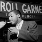 Szene aus dem Film "Misty - The Erroll Garner Story": Ein Mann zündet einem anderen eine Zigarette an. Im Hintergrund ist auf einer Werbetafel der Schriftzug "Erroll Garner" zu sehen. © 2024 FilmsGrandHuit 