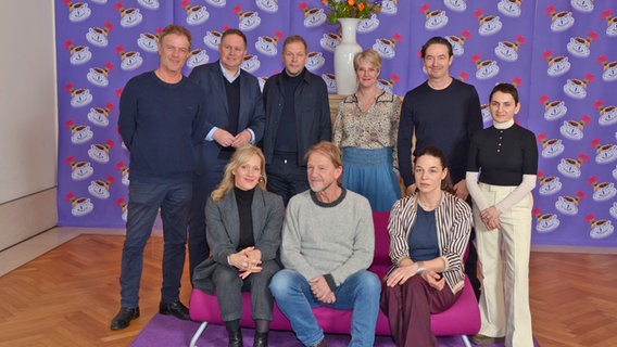 Eine Gruppe von Menschen in legerer Kleidung sitzt auf einem roten Sofa oder steht dahinter vor einer Tapete mit aufgedruckten Teetassen (das Filmteam der Produktion "Meine Ältern") © NDR Foto: Patricia Batlle