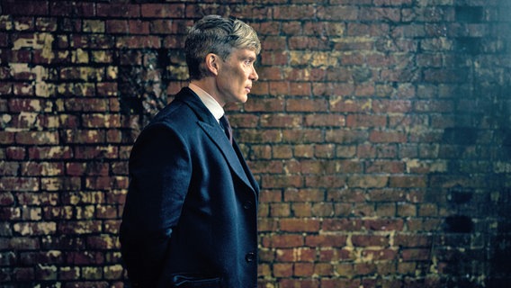 ein Mann mit dunklem Anzug steht seitlich vor einer Wand in Birmingham - Szene aus "Peaky Blinders" dem Kinofilm mit Cillian Murphy © Netflix / Robert Viglasky Photography Foto: Robert Viglasky