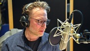 Ein Mann mit Brille spricht in ein Studio-Mikrofon - Der Schauspieler und Synchronsprecher Sascha Rotermund im Studio von NDR Kultur © NDR 