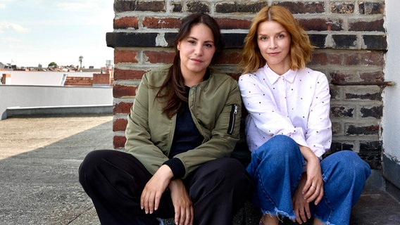 Zwei junge Frauen sitzen angelehnt an einen Ziegelwand - eine mit langen dunklen Haaren, eine andere mit rötlichen Haaren ( © NDR/Nordfilm/Marcus Höhn Foto: Marcus Höhn