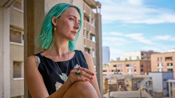 Eine junge Frau mit blauen Haaren sitzt auf einer Balustrade und schaut nachdenklich - Szene aus dem Drama "The Outrun" © STUDIOCANAL / The Outrun Ltd., Roy Imer Foto: Roy Imer